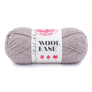 Pode incluir: Um novelo de lã Wool-Ease cinza claro. O rótulo diz "Wool Ease" com o logotipo da Lion Brand e ícones de floco de neve, chapéu e suéter. O fio é uma mistura de lã e outras fibras.