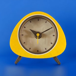 May include: A vintage yellow clock with a unique triangular design and brown legs. The clock face is white with black numerals and hands. The clock's yellow frame has a textured finish, and the hands indicate 10:08.