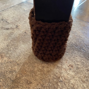 Può includere: Un proteggi-gambe per mobili marrone all'uncinetto. La copertura accogliente è progettata per adattarsi perfettamente attorno a una gamba di tavolo o sedia, fornendo una barriera morbida. La cucitura strutturata crea un accessorio decorativo e funzionale.