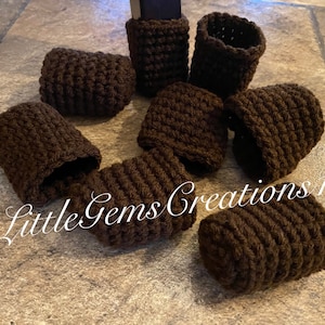 Può includere: Un set di otto protezioni per gambe di sedia in crochet marrone. Le protezioni sono realizzate in un filato morbido e testurizzato e sono progettate per proteggere le gambe dei mobili da graffi e danni.