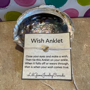 May include: White string anklet with a white shell bead. The anklet is tied around a card that reads "Wish Anklet" and includes instructions: "Close your eyes and make a wish, Then tie this Anklet on your ankle. When it falls off or wears through, that is when your wish comes true." The card is signed "Lil Gems Jewelry Canada."
