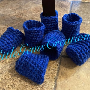 May include: A set of blue crocheted chair leg protectors. The protectors are made of a soft, textured yarn and are designed to protect furniture legs from scratches and damage.  The protectors are shown on a tiled floor.