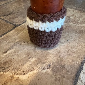 May include: Brown crocheted furniture leg covers with a white band. The covers are protecting the wooden legs from scratches.