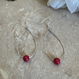 May include: A pair of silver dangle earrings with a red bead on each earring.