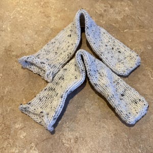 Könnte beinhalten: Ein Paar weiße Stricksocken mit schwarzen Flecken. Die Socken sind in Dreiecksform gefaltet.