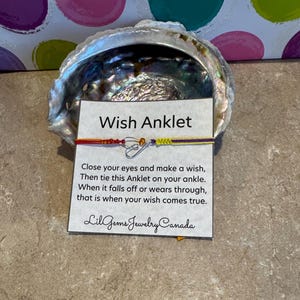 May include: A colourful wish anklet with a silver heart charm and the text "Wish Anklet" on a white card. The card also includes instructions on how to use the anklet and the text "Close your eyes and make a wish, Then tie this Anklet on your ankle. When it falls off or wears through, that is when your wish comes true. Lil Gems Jewelry Canada".