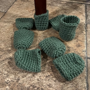 May include: A set of eight green crocheted furniture leg protectors. The protectors are round and have a textured surface.