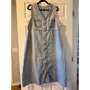 Può includere: Un abito smanicato in denim azzurro con scollo a V, chiusura frontale con bottoni per tutta la lunghezza e due tasche sul petto. Il capo è realizzato con un lavaggio denim più chiaro sul corpetto e uno leggermente più scuro sulla gonna.