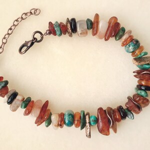 May include: A multi-colored gemstone bracelet with a copper chain clasp. The bracelet features a variety of stones, including turquoise, amber, and carnelian.