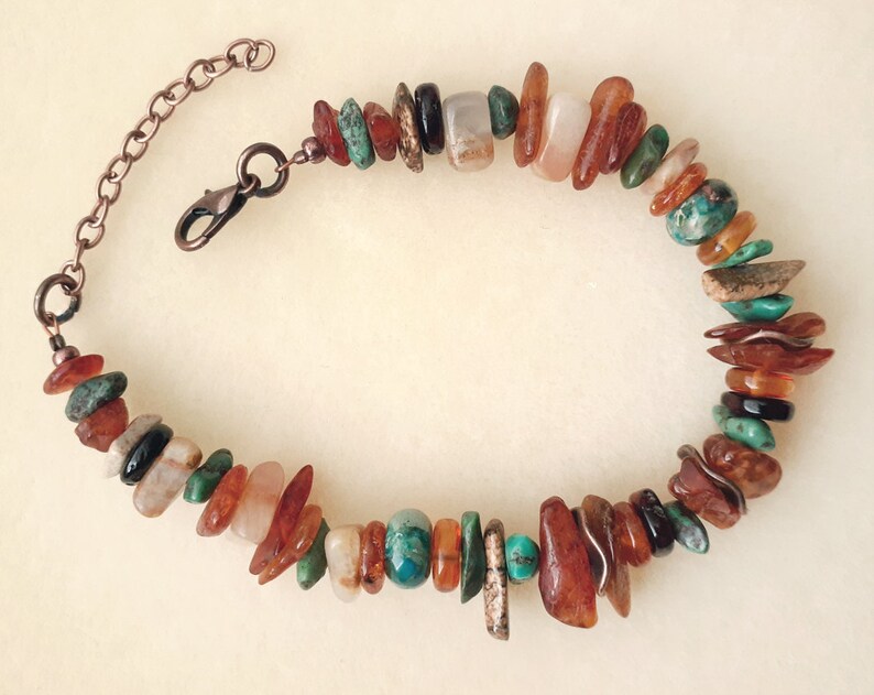 May include: A multi-colored gemstone bracelet with a copper chain clasp. The bracelet features a variety of stones, including turquoise, amber, and carnelian.