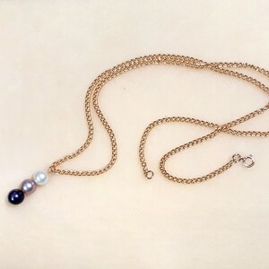May include: A gold chain necklace with a pendant featuring three pearls in black, gray, and white.