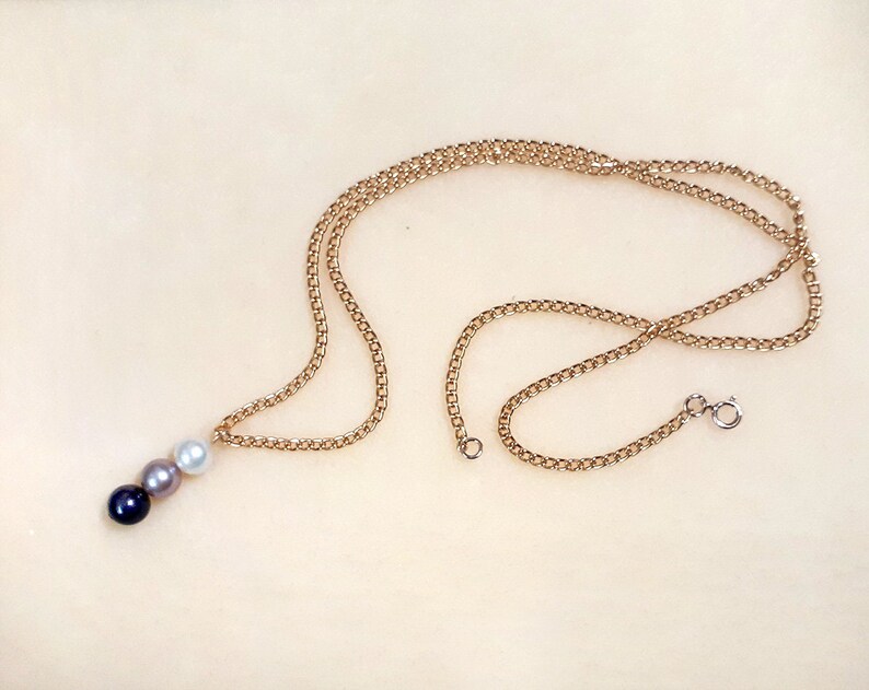 May include: A gold chain necklace with a pendant featuring three pearls in black, gray, and white.