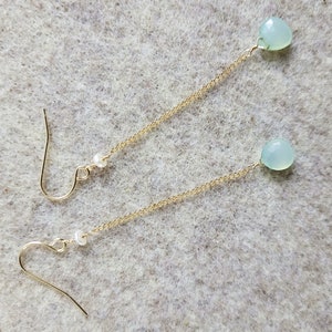 May include: A pair of long, delicate gold chain earrings with a light blue gemstone and a white pearl on each chain.