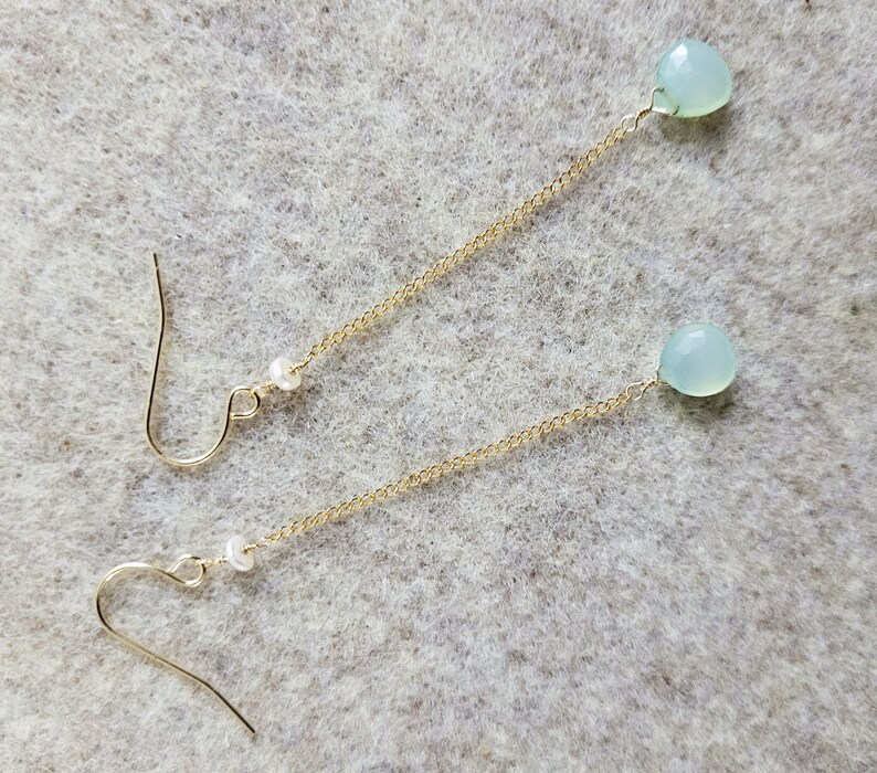 May include: A pair of long, delicate gold chain earrings with a light blue gemstone and a white pearl on each chain.