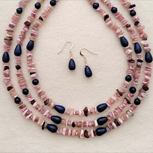 May include: A three-strand necklace made of pink and brown stones with dark blue accents. Matching earrings with dark blue stones hang from gold hooks.