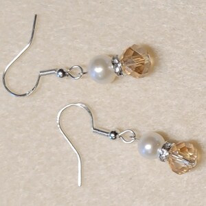 May include: A pair of silver earrings with a white pearl and a clear amber crystal bead.
