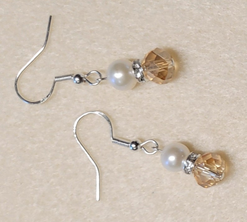May include: A pair of silver earrings with a white pearl and a clear amber crystal bead.