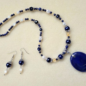 May include: A blue lapis lazuli pendant necklace with a silver clasp and matching earrings. The necklace features blue, white, and gold beads.
