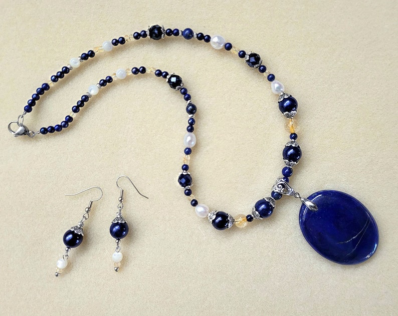 May include: A blue lapis lazuli pendant necklace with a silver clasp and matching earrings. The necklace features blue, white, and gold beads.