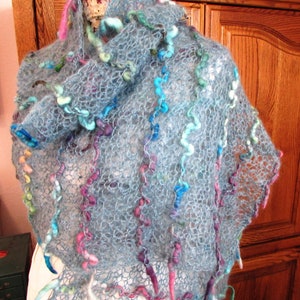 May include: A light blue crocheted shawl with colorful yarn accents. The shawl is made with a delicate openwork stitch and features long, flowing strands of yarn.