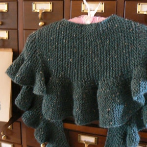 May include: A teal knitted shawl with ruffled edges, hanging on a wooden cabinet with brass hardware.