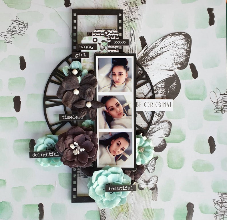 May include: A scrapbook page with a collage of photos, flowers, and decorative elements. The page features a black film strip frame with three photos of a person. There are paper flowers in shades of gray and teal, and butterfly accents. Text includes "happy girl", "timeless", "delightful", "beautiful", "xoxo", and "BE ORIGINAL".