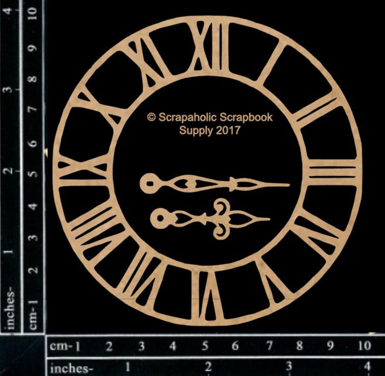 May include: A laser-cut wooden clock face with Roman numerals and two separate clock hands. The clock face is circular with the text "Scrapaholic Scrapbook Supply 2017". The clock face measures approximately 4 inches in diameter.