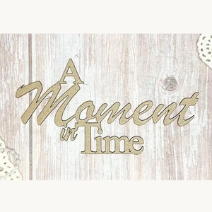 以下が含まれることがあります： 「A Moment in Time」という言葉が筆記体で書かれた木製の切り抜き。文字は薄茶色で、背景は明るい木目模様です。クラフトや家の装飾に適しています。