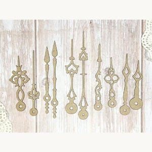 Puede incluir: Una colección de once manecillas de reloj cortadas con láser en varios estilos decorativos. Las manecillas son de madera marrón claro y presentan diseños intrincados, incluyendo puntas de flecha, corazones y formas geométricas. Están dispuestas sobre un fondo de vetas de madera clara.