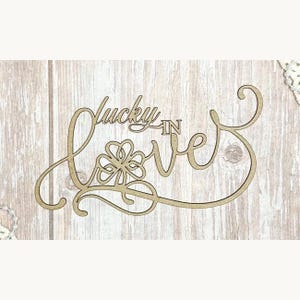 May include: A wooden sign reading "Lucky in Love" in a cursive font. The word "Love" incorporates a shamrock design. The sign is crafted from light brown wood and is set against a light wood background.