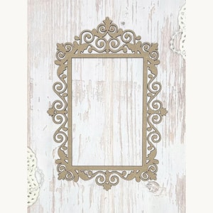 May include: A decorative, rectangular wooden frame with an ornate, swirling design. The frame is a light brown color and has a rectangular opening in the center. The frame is set against a white, weathered wood background.