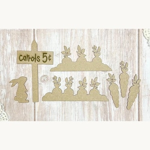 Op de afbeelding: Een verzameling onafgewerkte houten paasuitsparingen. Bevat een bord met de tekst "Wortels 5¢", een konijnensilhouet, wortelvormen en rijen wortels met loof. Perfect voor knutselen en seizoensdecoratie.
