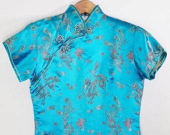 Könnte beinhalten: Ein türkisblaues Seiden-Cheongsam-Kleid mit goldenen und silbernen Stickereien von Drachen und Blumen.