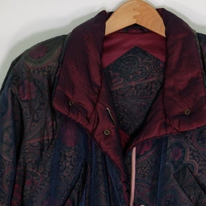 May include: A dark blue and burgundy paisley patterned jacket with a zipper closure and a burgundy lining. The jacket has a stand-up collar and a button closure at the neck.