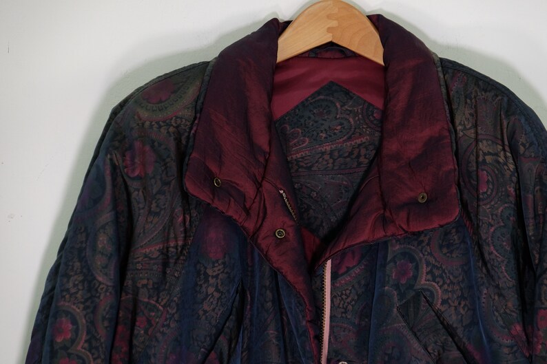 May include: A dark blue and burgundy paisley patterned jacket with a zipper closure and a burgundy lining. The jacket has a stand-up collar and a button closure at the neck.