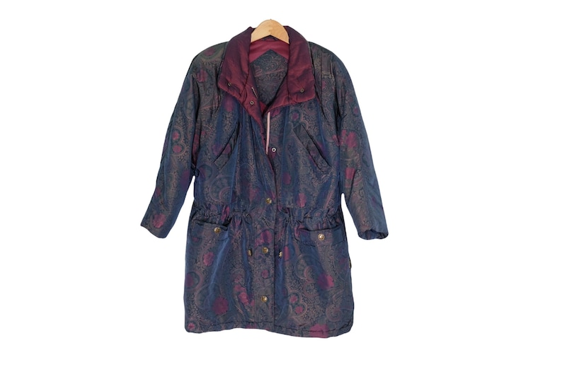 May include: A long-sleeved, blue and purple patterned jacket with a drawstring waist and a zipper closure. The jacket has a hood and two pockets.