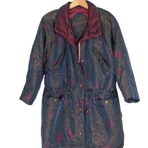 May include: A long, blue and burgundy patterned jacket with a drawstring waist and a zipper closure. The jacket has a paisley design and is hanging on a wooden hanger.