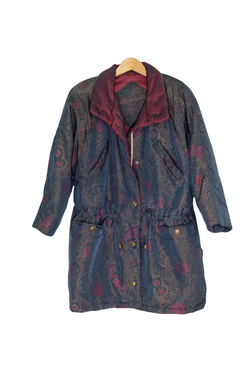May include: A long, blue and burgundy patterned jacket with a drawstring waist and a zipper closure. The jacket has a paisley design and is hanging on a wooden hanger.