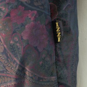 May include: A black fabric with a paisley pattern in shades of pink, green, and brown. The fabric has a black label with the word "IZZI" in gold lettering.