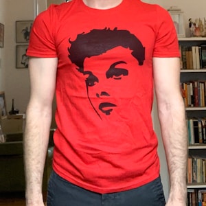 May include: A red t-shirt with a black and white silhouette of a person's face on the front.