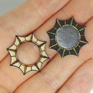 Puede incluir: Dos formas de sol de madera con un borde dorado. Un sol tiene un centro plateado y el otro tiene un centro de madera.