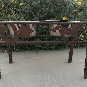 Könnte beinhalten: Ein rustikaler Metall-Futternapf mit zwei Edelstahlnäpfen. Der braune Metallrahmen hat ein Hufeisen, einen Stern und eine Pferdesilhouette. Die Beine haben ein gedrehtes Bewehrungsdesign.