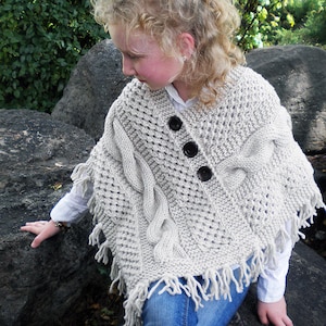 May include: A light gray knitted poncho with a cable knit design and fringe trim. The poncho has three black buttons down the front. The text "Back to School Poncho" is written below the image.
