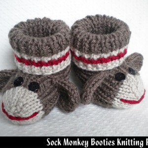 Puede incluir: Botas de bebé tejidas en forma de monos de calcetines. Las botas son grises con rayas rojas y blancas y tienen ojos de botón negros.