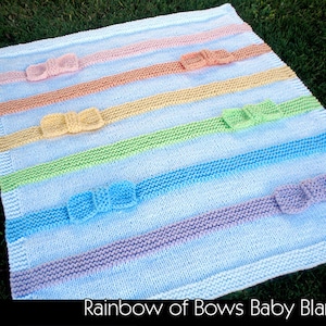 May include: A knitted baby blanket with a rainbow of colors and bows. The blanket is made with a light blue yarn and has stripes of pink, orange, yellow, green, blue, and purple. The bows are made with the same yarn as the stripes.