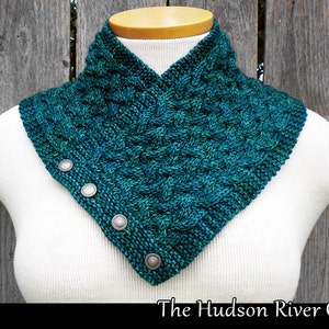 May include: A teal blue knitted cowl with a cable knit pattern and silver buttons. The cowl is displayed on a white mannequin against a wooden background. The text "The Hudson River Cowl" is displayed below the cowl.