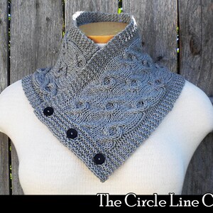 Könnte beinhalten: Ein grauer Strickkragen mit einem Zopfmuster und drei schwarzen Knöpfen. Der Kragen wird auf einer weißen Puppe vor einem hölzernen Hintergrund gezeigt. Der Text "The Circle Line Cowl" wird unter dem Kragen angezeigt.