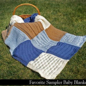 May include: A multi-colored knitted baby blanket with different stitch patterns in shades of blue, brown, and white. The blanket is laid out on a bed of green grass.
