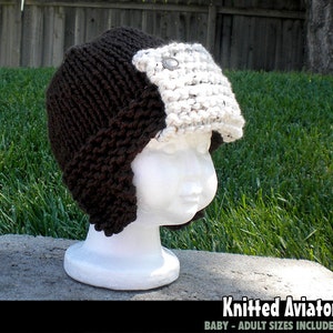 May include: Knitted aviator hat with a brown brim and a white fleece earflap. The hat is displayed on a white mannequin head.