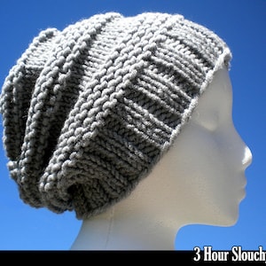 May include: A gray slouchy knit hat on a white mannequin head. The hat is made with a simple knit stitch and has a relaxed, slouchy fit.